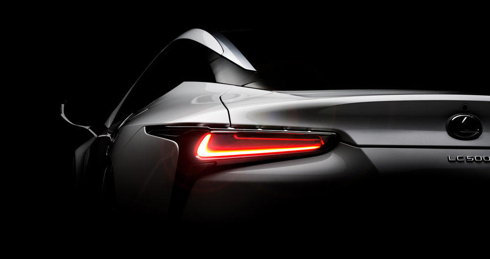 Rear view of a silver Lexus LC 500 car in a dark studio setting, highlighting its sleek design and taillights.