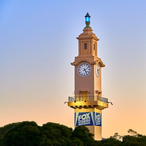 Fox Studios Australia clock tower in Sydney, featuring vintage-style architecture and illuminated details against a clear sky.