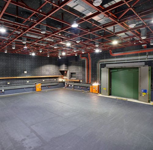 Wide angle shot of an empty sound stage with overhead lighting and a green door visible in the background, no people are present.