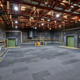 Wide view of a large industrial warehouse stage with high red metal truss ceiling and grid of overhead lights.