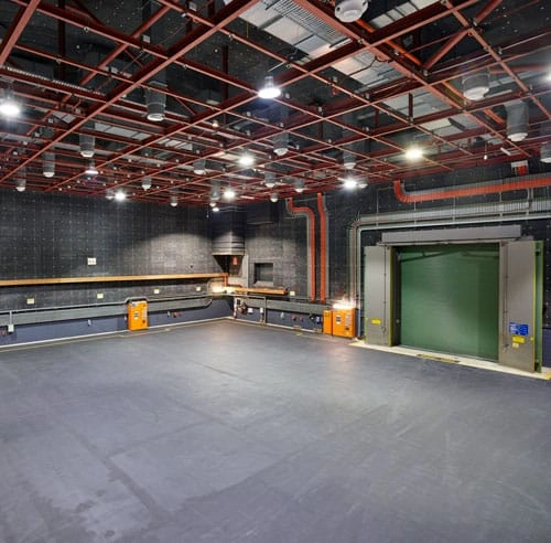 Wide view of a large commercial sound stage interior with exposed red steel ceiling grid and green acoustic doors.