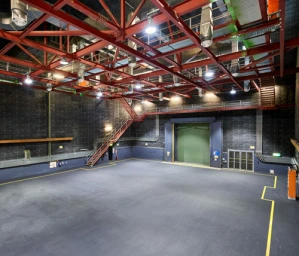Wide view of a large sound stage interior with red steel ceiling trusses, catwalks, dark acoustic walls, and a large cargo door