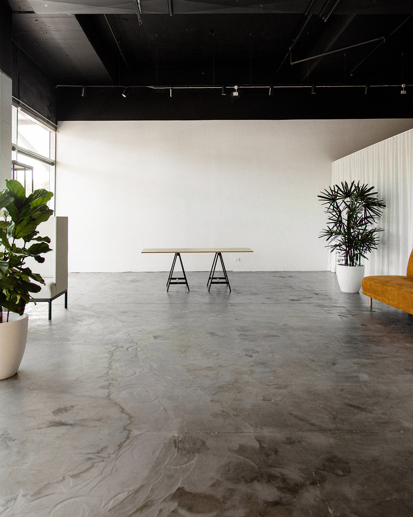 Spacious interior featuring a tan table on black sawhorses, a gray polished concrete floor, and lush green plants in white pots.
