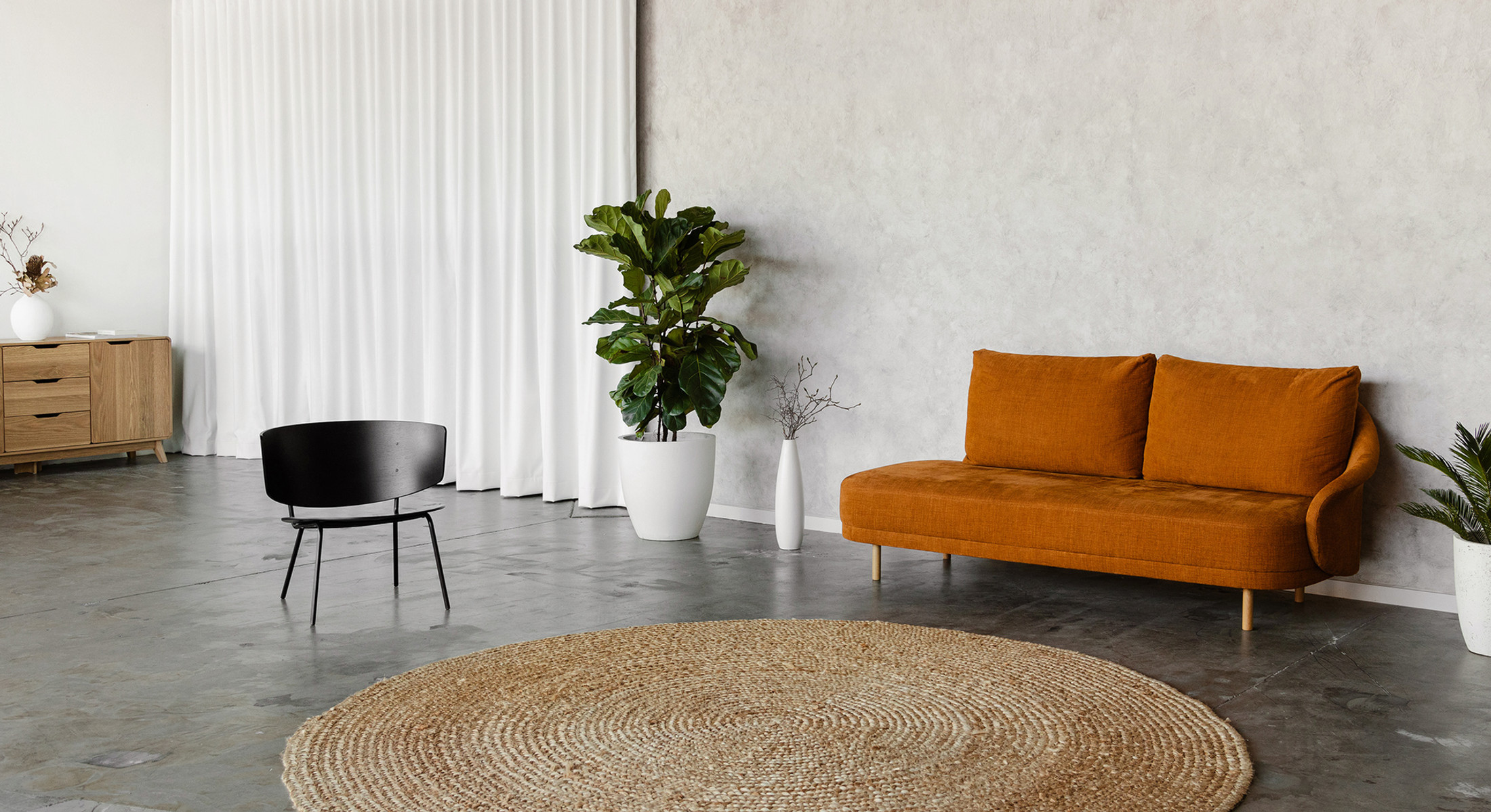 Interior space features an orange sofa, black chair, and lush potted plant against a neutral backdrop, enhanced by a circular rug.
