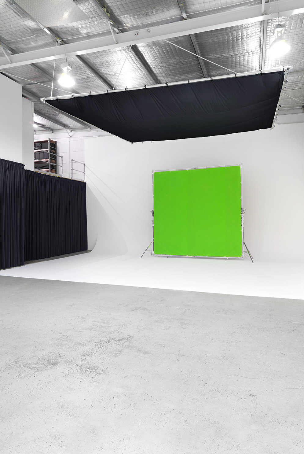 An empty photo studio features a green screen, black curtains, and studio lighting, ideal for video production and photography projects.