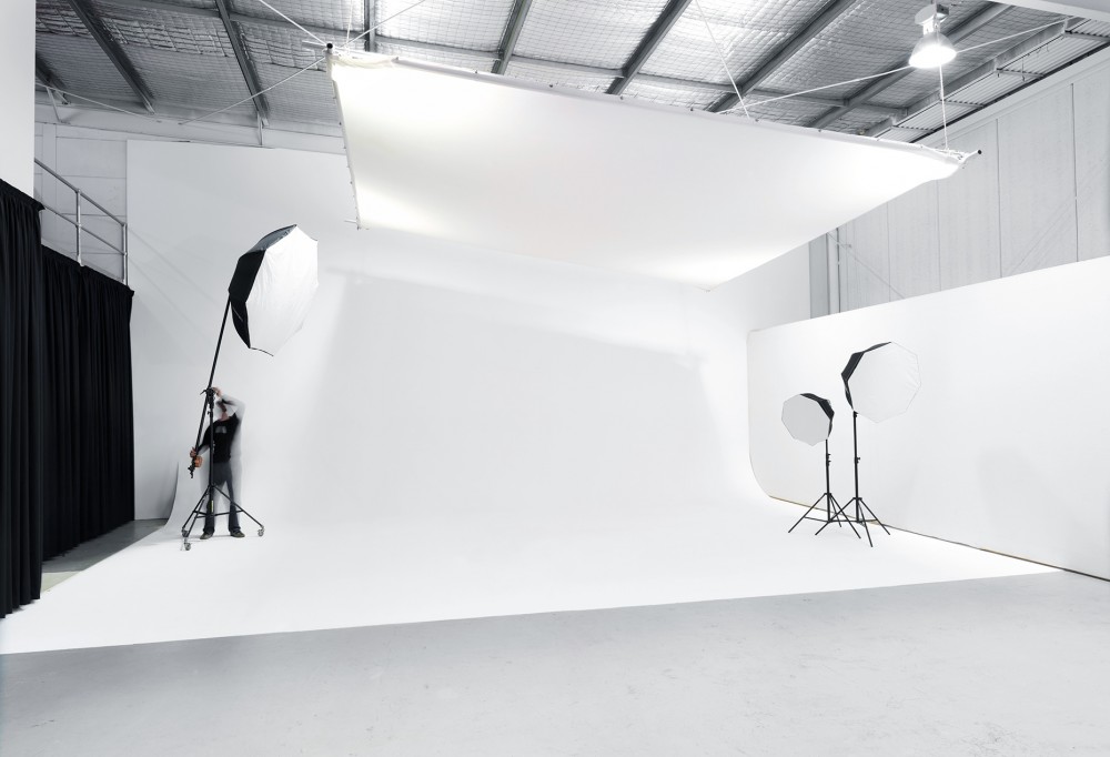 Wide view of a photo studio featuring a white backdrop, lighting equipment, and a technician adjusting a light, highlighting the controlled environment.