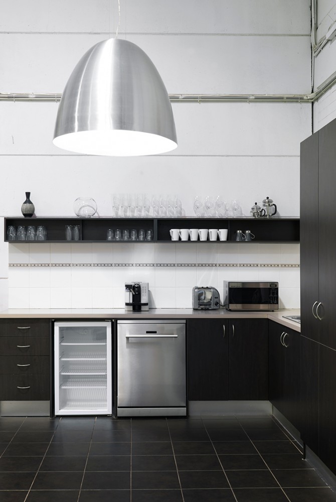 Modern kitchen interior with stainless steel appliances, dark cabinets, tiled floor, pendant light, and glassware on shelving.