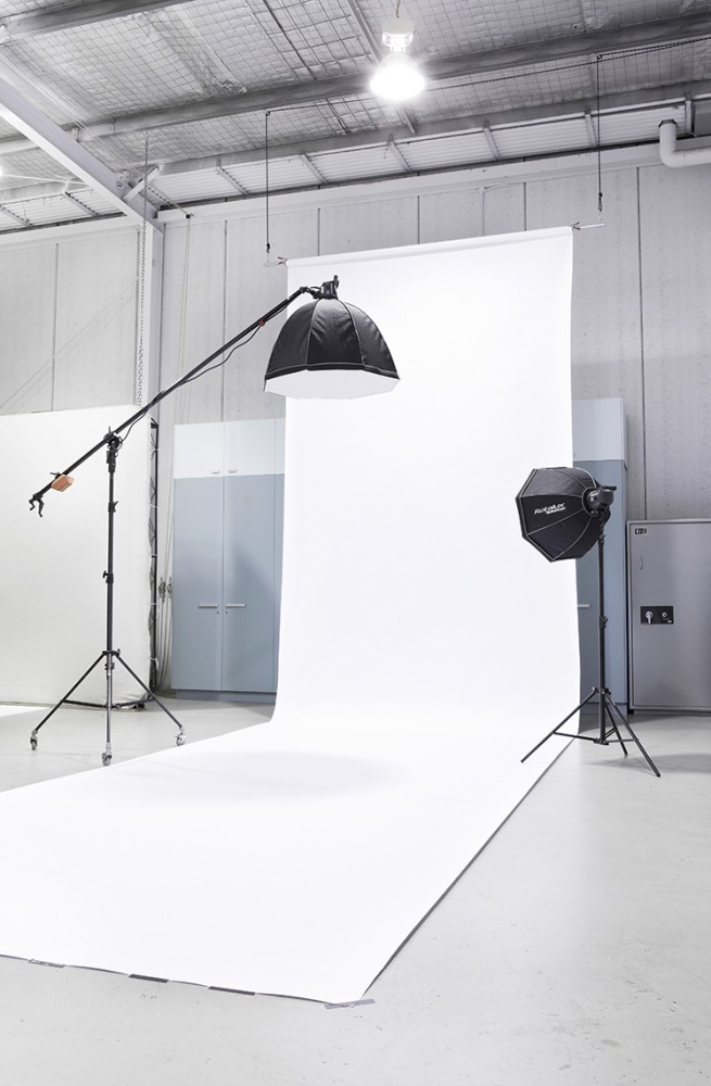 Photo studio setup featuring lighting equipment and a large white backdrop, providing a professional and clean environment for photography.