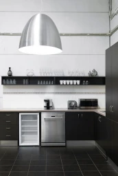 Modern commercial kitchen interior with dark cabinets, stainless steel appliances, and a large dome pendant light by Hatch Studios