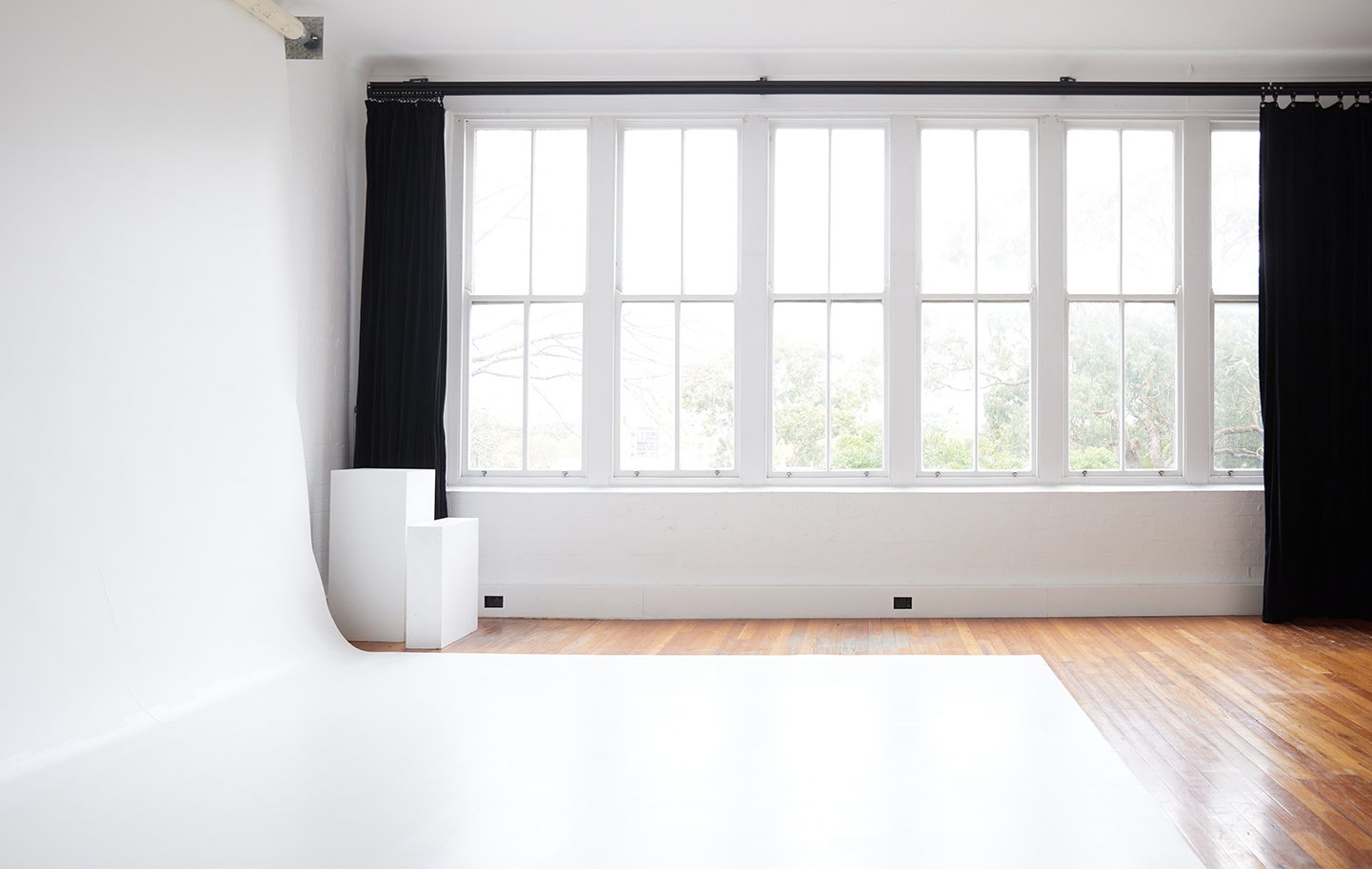 Bright photo studio with a white backdrop, natural light from large windows, and simple geometric platforms for product or portrait shoots.