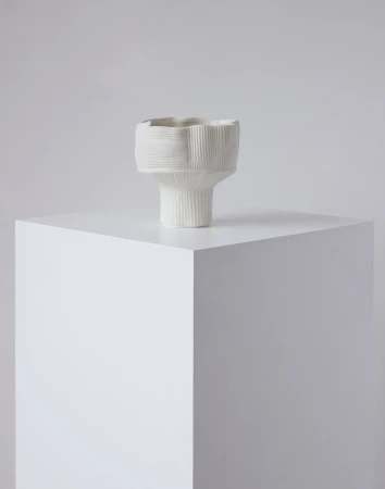 White textured ceramic vessel resting on a matching white plinth against a neutral background