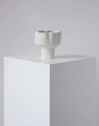 White textured ceramic vessel resting on a matching white plinth against a neutral background