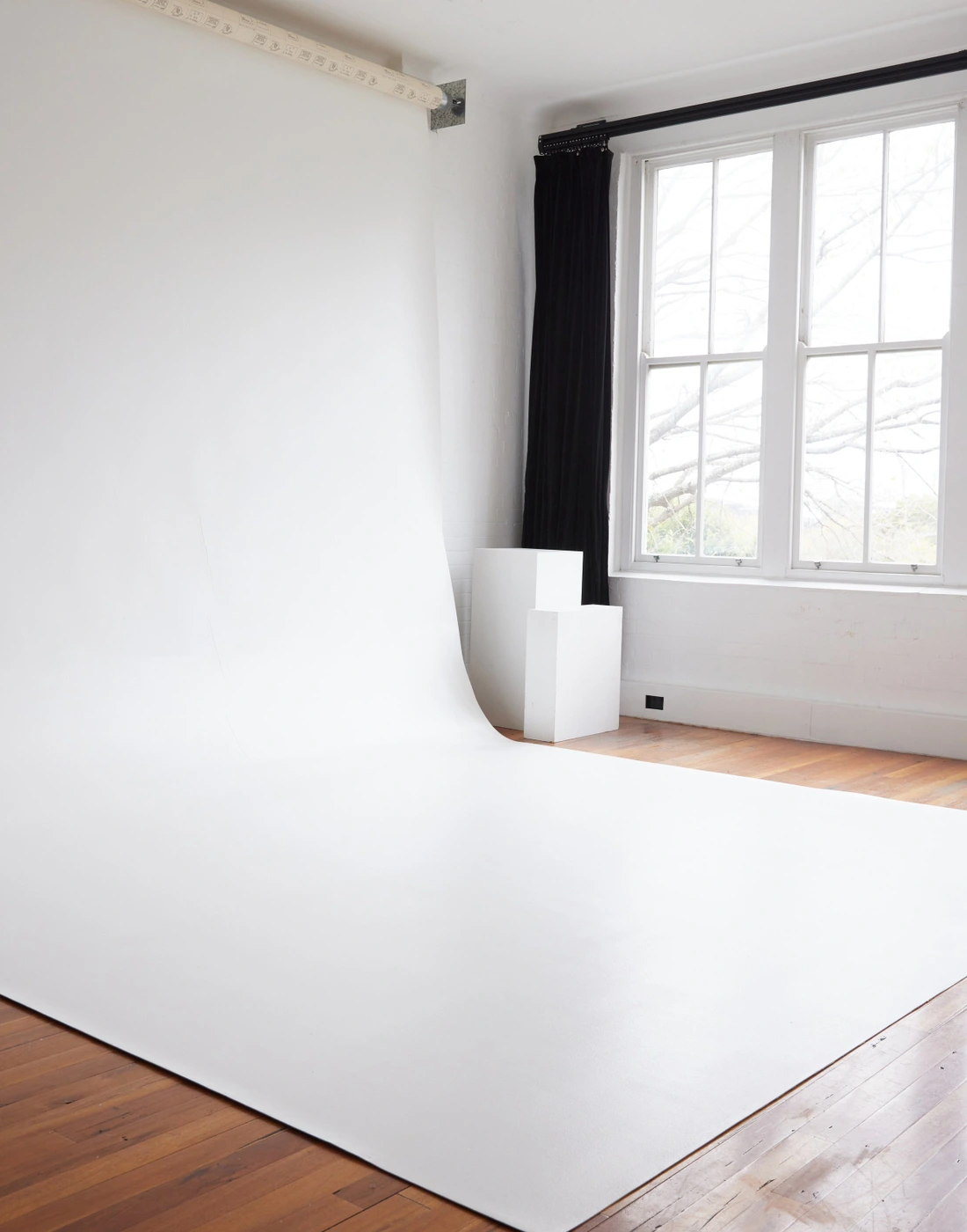 Empty white photo studio cyclorama wall with wooden floors and a large multi-pane window in Brisbane