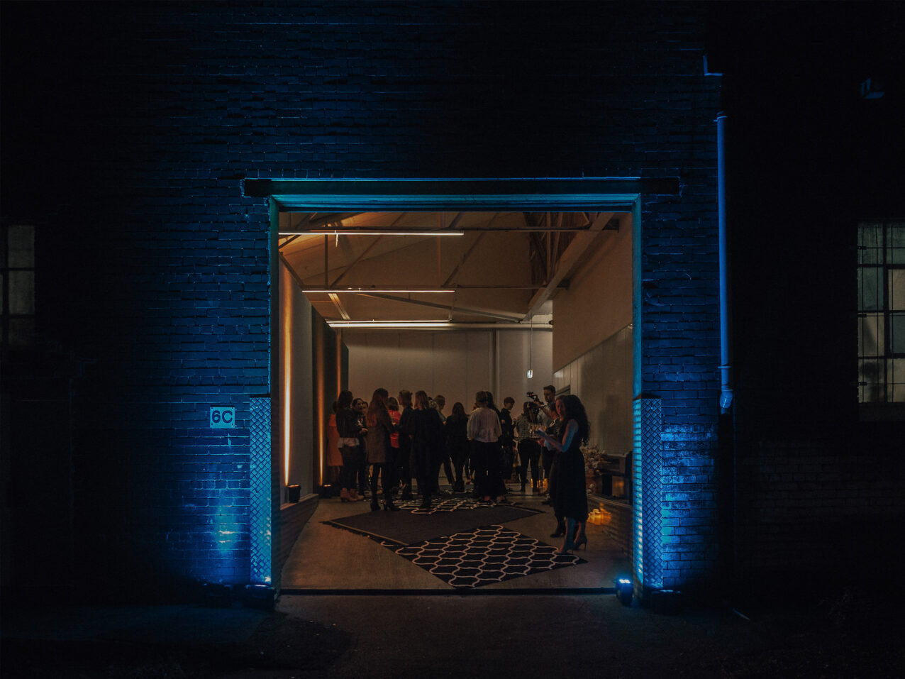 A group of people gather in an indoor setting at night, illuminated by indoor lighting, captured from a low angle with a wide shot.