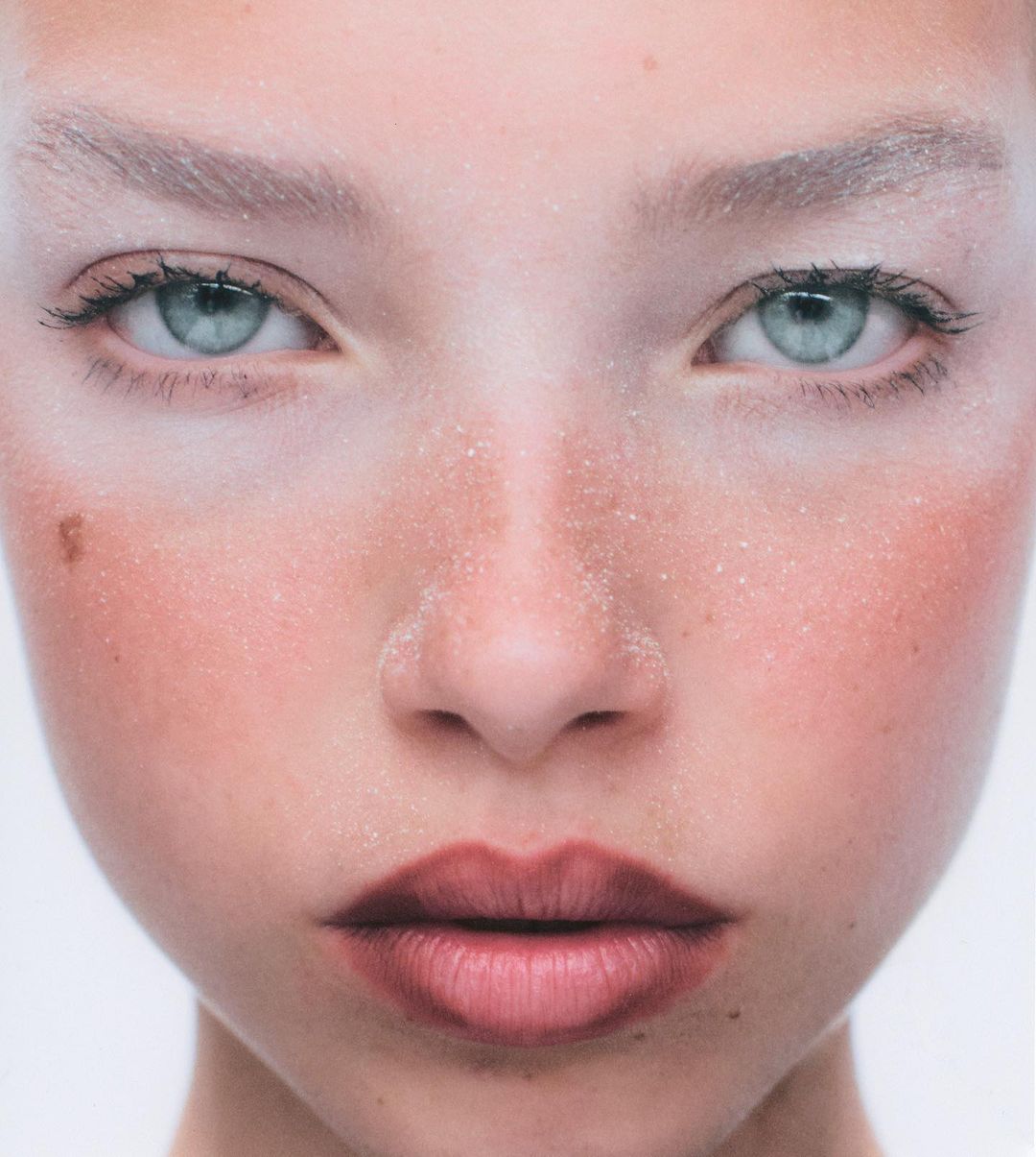 Close-up portrait of a young adult female with light skin, grey-blue eyes, and red lips with diffused lighting in a minimalist white studio.