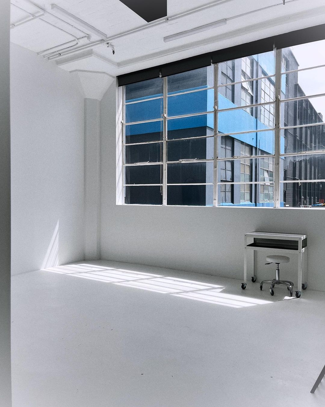 Bright photo studio with white walls, large window, industrial design elements, minimalist furniture, and natural light. Ideal for creatives.