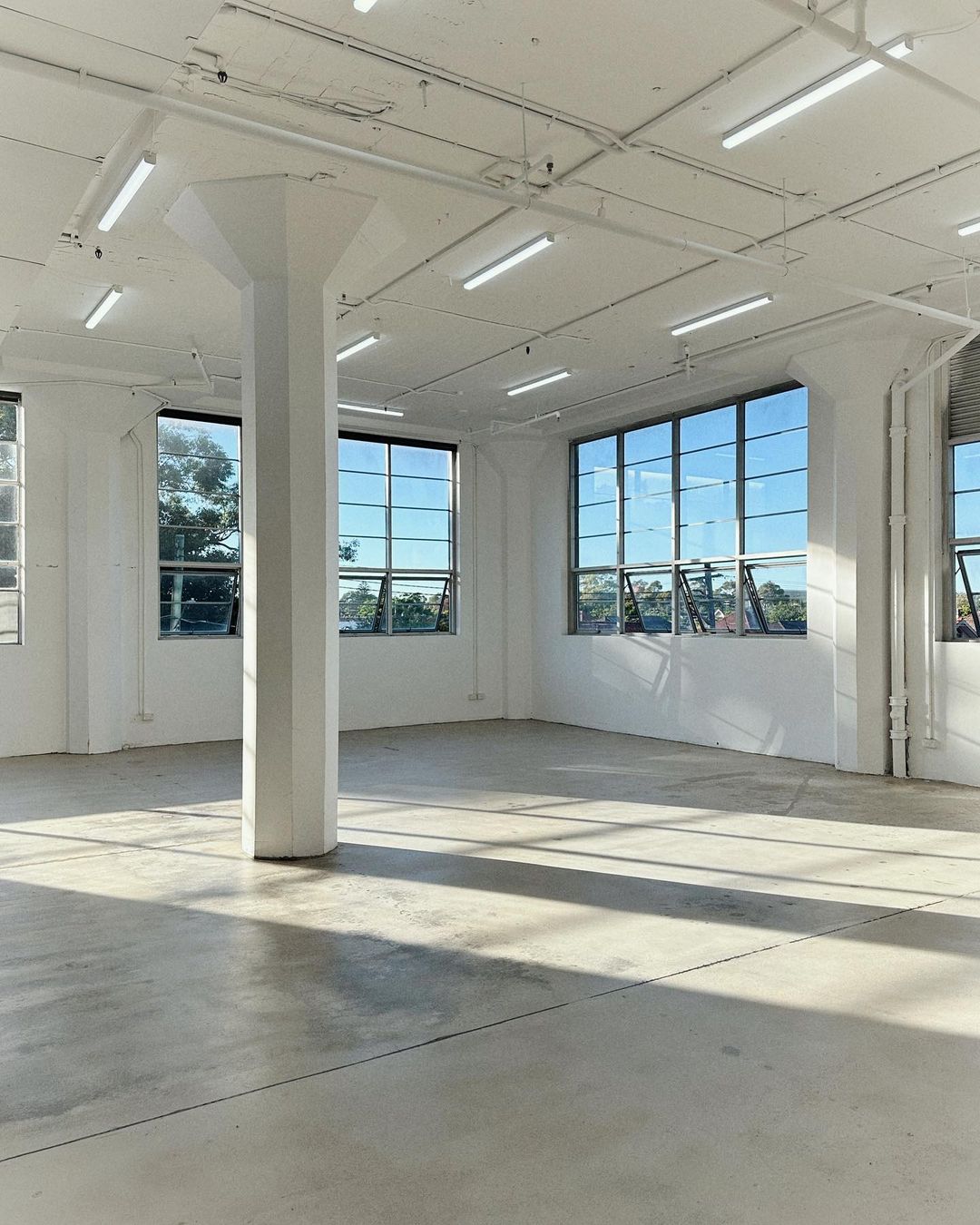 Wide angle view of empty white industrial room with polished concrete floors and large windows with natural light in commercial space.