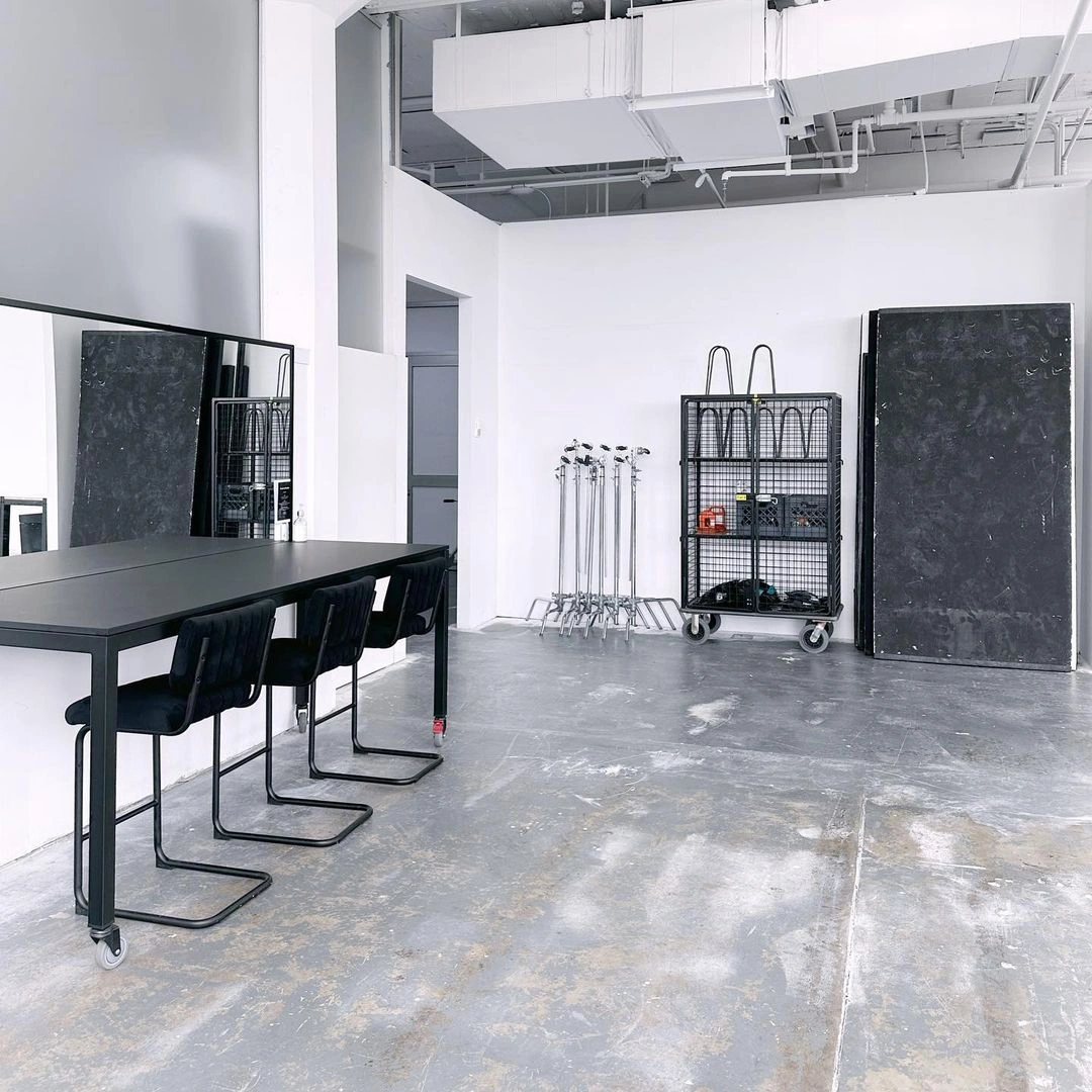 Spacious photo studio in Sydney with a long black table, modern chairs, a rolling storage cart, and white walls.