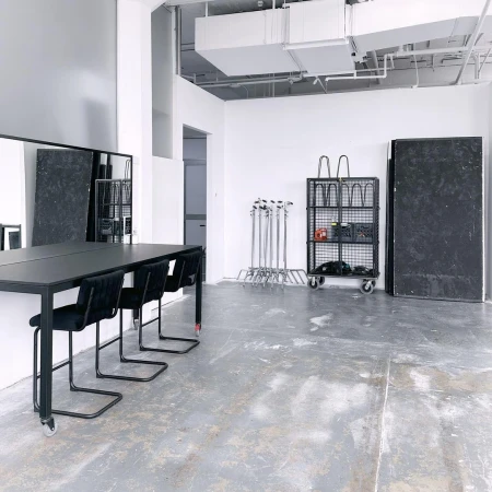 Spacious photo studio in Sydney with a long black table, modern chairs, a rolling storage cart, and white walls.