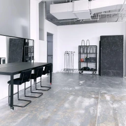 Spacious photo studio in Sydney with a long black table, modern chairs, a rolling storage cart, and white walls.