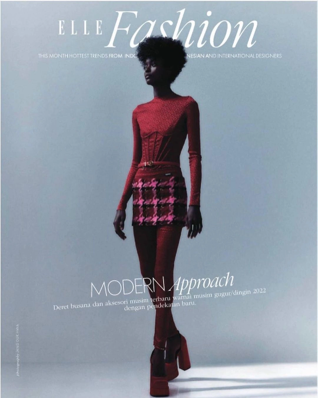 Black model in red long-sleeve top and patterned miniskirt with platform heels standing against a grey background