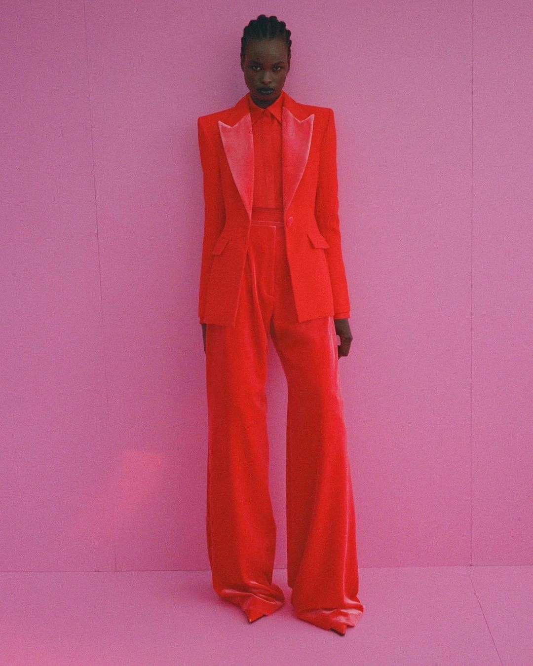 Model wearing a vibrant red suit standing against a textured pink background in a studio portrait by Rosebery Studios