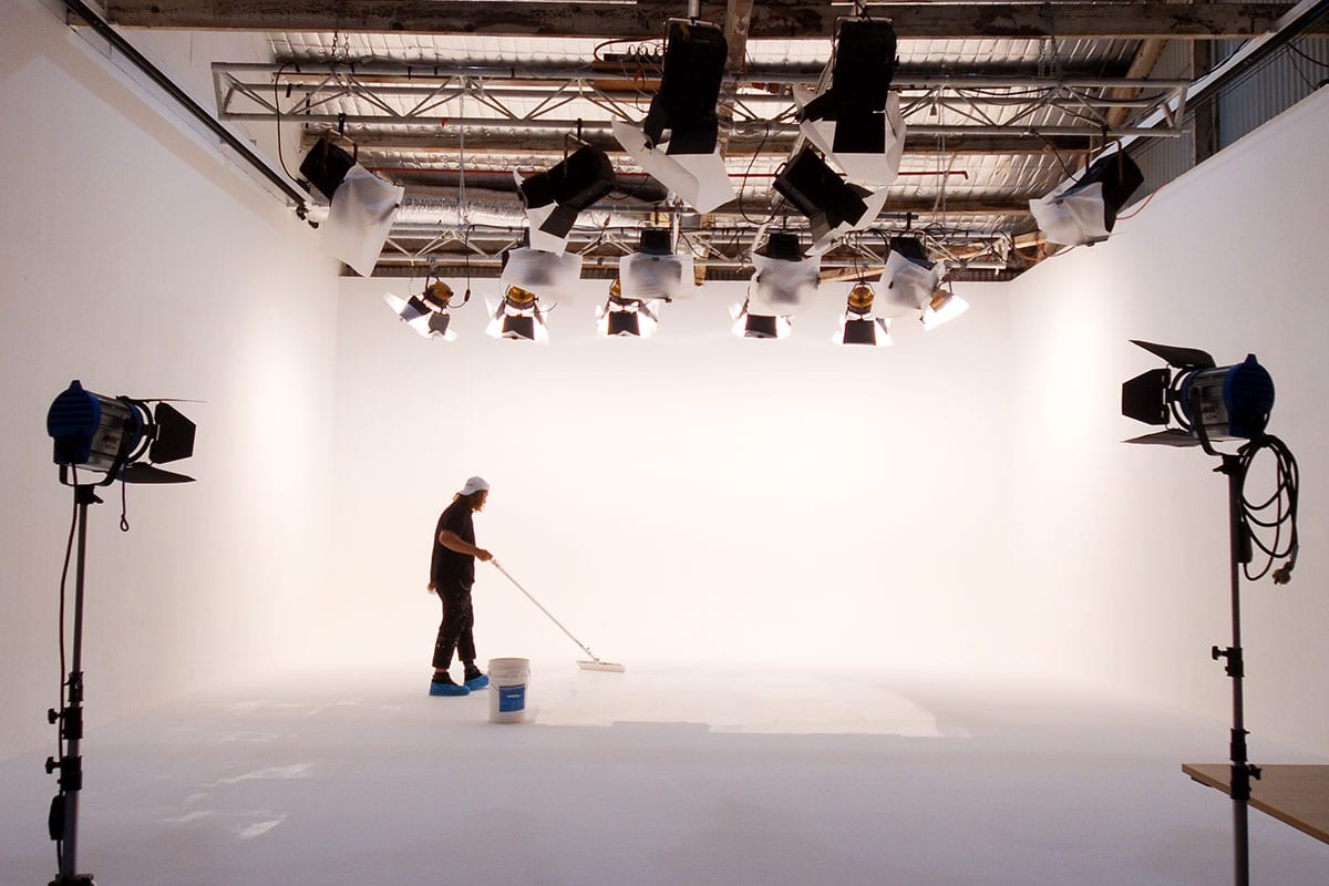 Photo studio interior with a person mopping the floor. Overhead lighting rig and white backdrop define the professional workspace.