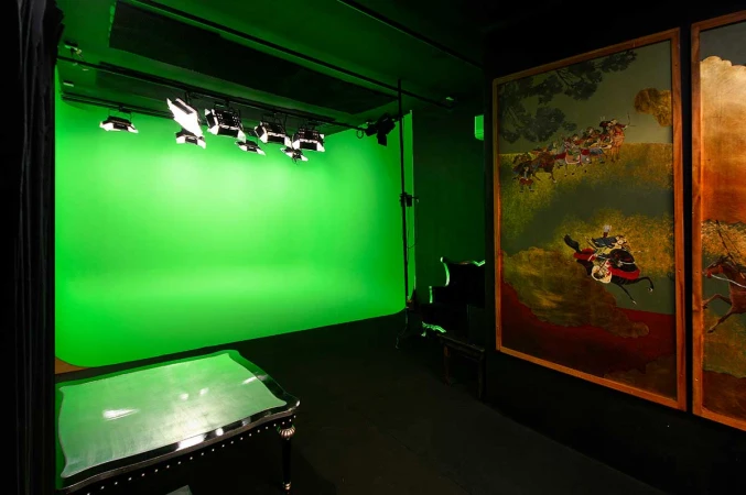 Photo studio with a green screen, lighting equipment, black stage, and vintage art panels creating a versatile creative space.