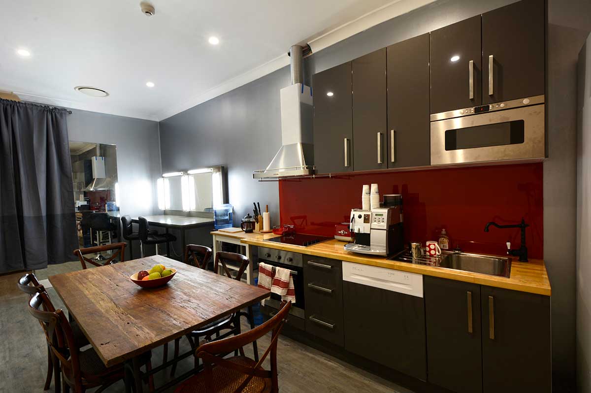 Modern kitchen and makeup room with dining table. Gray cabinets, red backsplash, and vanities with illuminated mirrors.