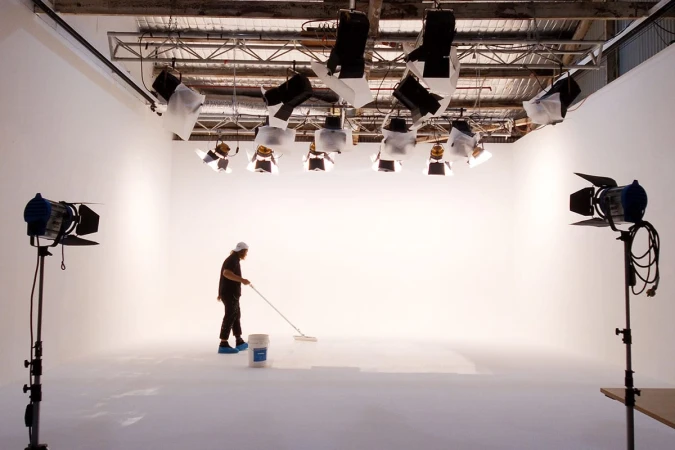 A person painting a white seamless studio floor beneath an overhead lighting rig at Sydney Props Studios.