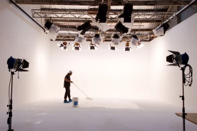 A person painting a white seamless studio floor beneath an overhead lighting rig at Sydney Props Studios.