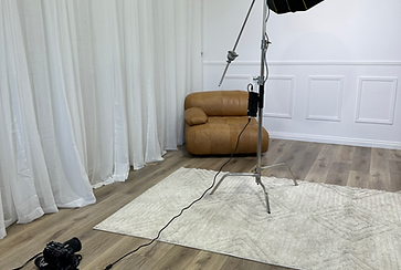 Photo studio setup with a tan leather armchair, softbox lighting equipment, and a white backdrop for professional photography.