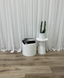 Minimalist white interior setup with two small round tables, books, and a potted cactus against sheer white curtains.