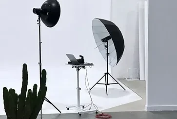 Professional photography studio setup with lighting equipment, camera, and laptop on a rolling cart