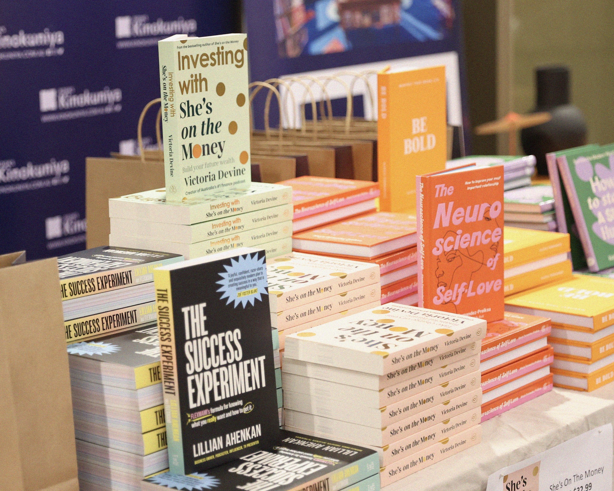 Display of personal finance and self-help books including 'Investing with She's on the Money' by Victoria Devine and 'The Success Experiment'.