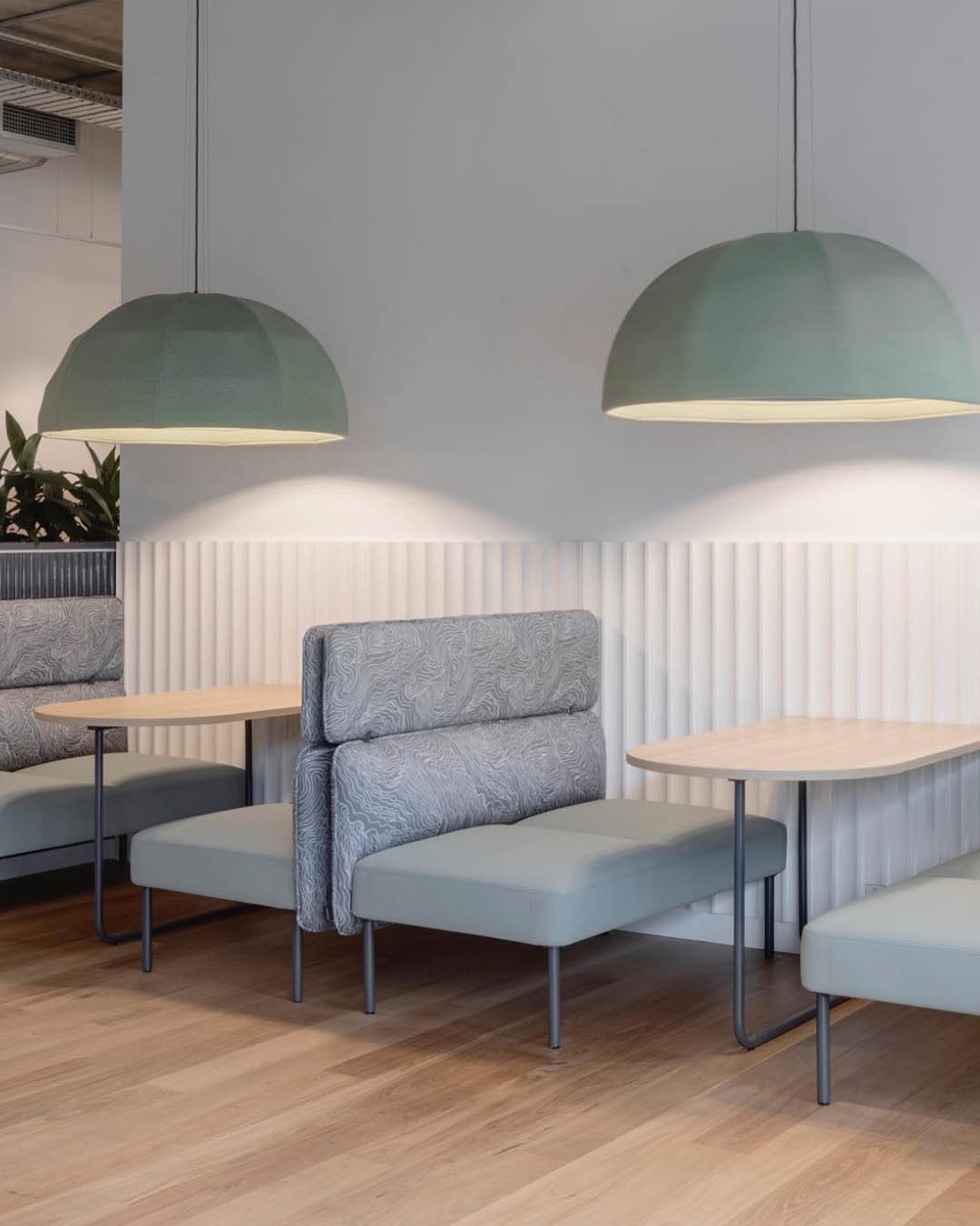 Contemporary office lounge area features light-green chairs, light-wood tables, and dome pendant lighting over light-wood flooring.