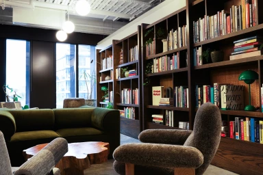 Modern office lounge featuring dark wood bookshelves filled with books, green sofa, and textured armchairs in Sydney.