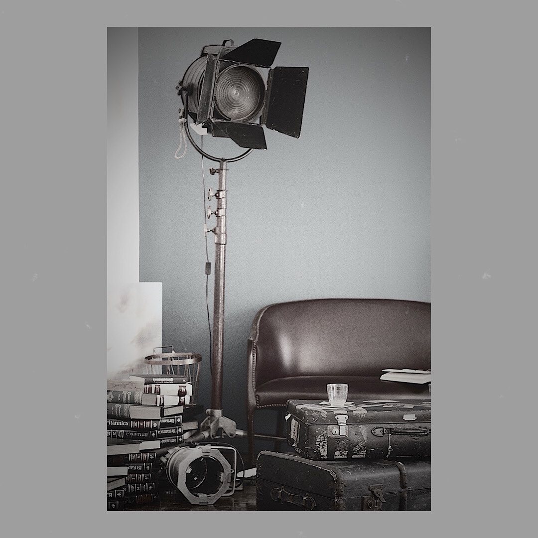 Vintage film set scene: An old movie spotlight on a stand, antique suitcases, and books create a nostalgic atmosphere indoors.