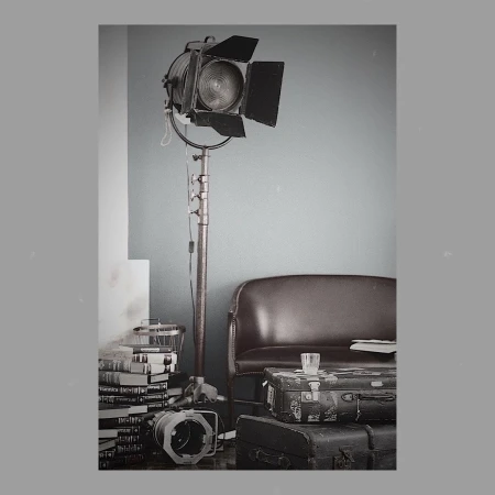 Vintage film set scene: An old movie spotlight on a stand, antique suitcases, and books create a nostalgic atmosphere indoors.