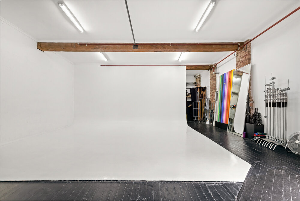 Empty photo studio with a cyclorama wall, white backdrop, and professional lighting equipment, ready for a photoshoot or video production.