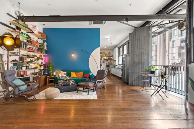 Eclectic living room interior with hardwood floors, vintage furniture, turquoise accent wall, and natural light, offering a cozy yet stylish space.