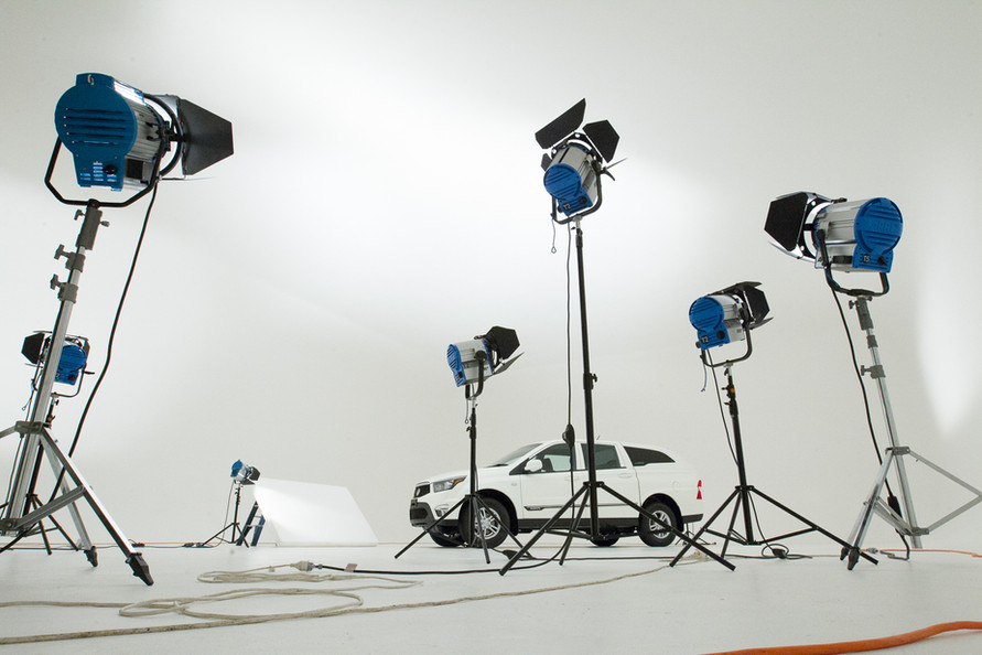 Automotive photoshoot in a photo studio with lighting equipment surrounding a white SUV on a white seamless backdrop.