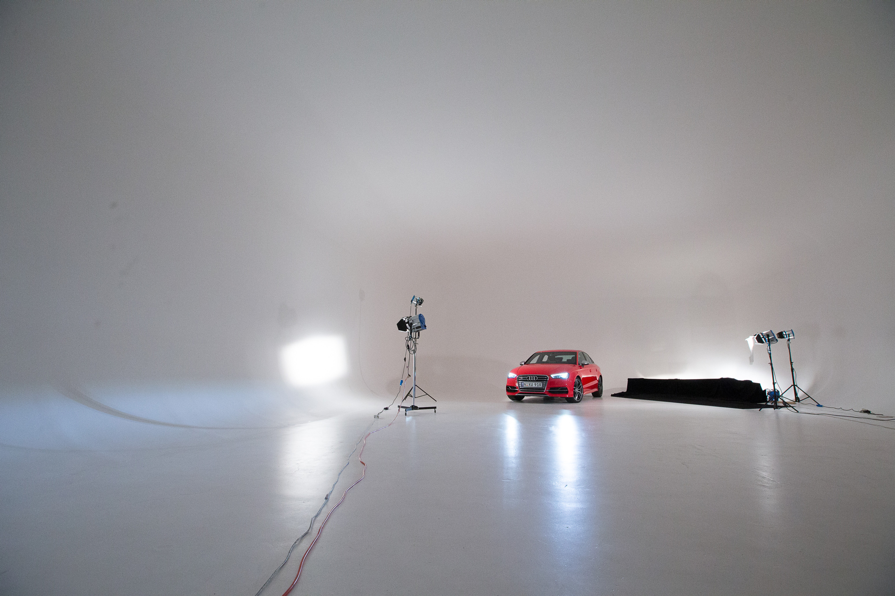 Red sedan car in a photo studio, illuminated by studio lighting, against a grey background. Automotive promotional visual.