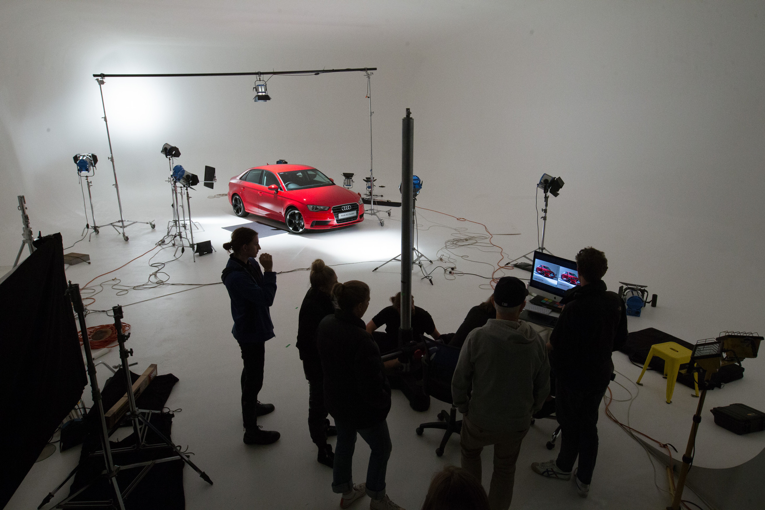 Bright red Audi sedan is photographed in a studio with photography crew and lighting equipment visible around the vehicle.