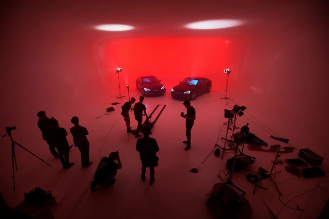 Automotive photoshoot in a studio with two black Tesla cars positioned under bright spotlights and a team of photographers.