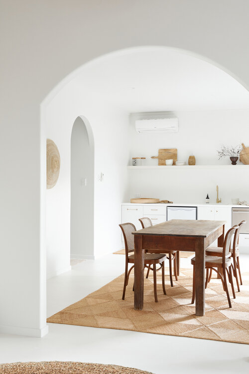Interior view of a bright, modern kitchen with a wooden dining table and chairs set on a natural fiber rug in a clean, minimalist space.