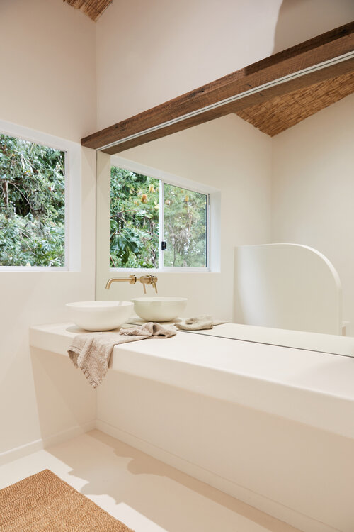Modern bathroom interior featuring white basin sinks, a large mirror, and green foliage visible through the window, creating a serene spa atmosphere.