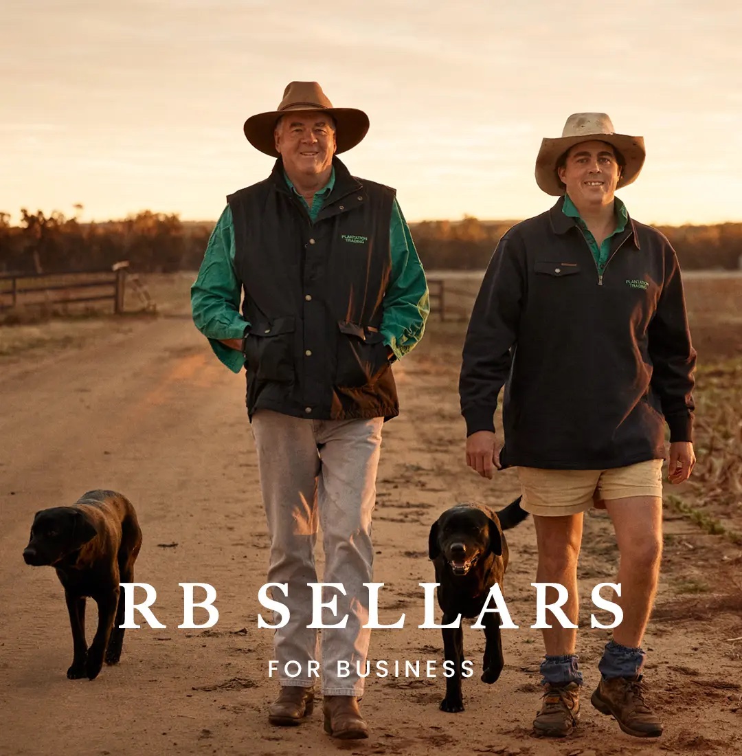 Two adult men in hats walk with dogs on a dirt road at sunset on a farm, wearing outdoor clothing, creating a rural scene.