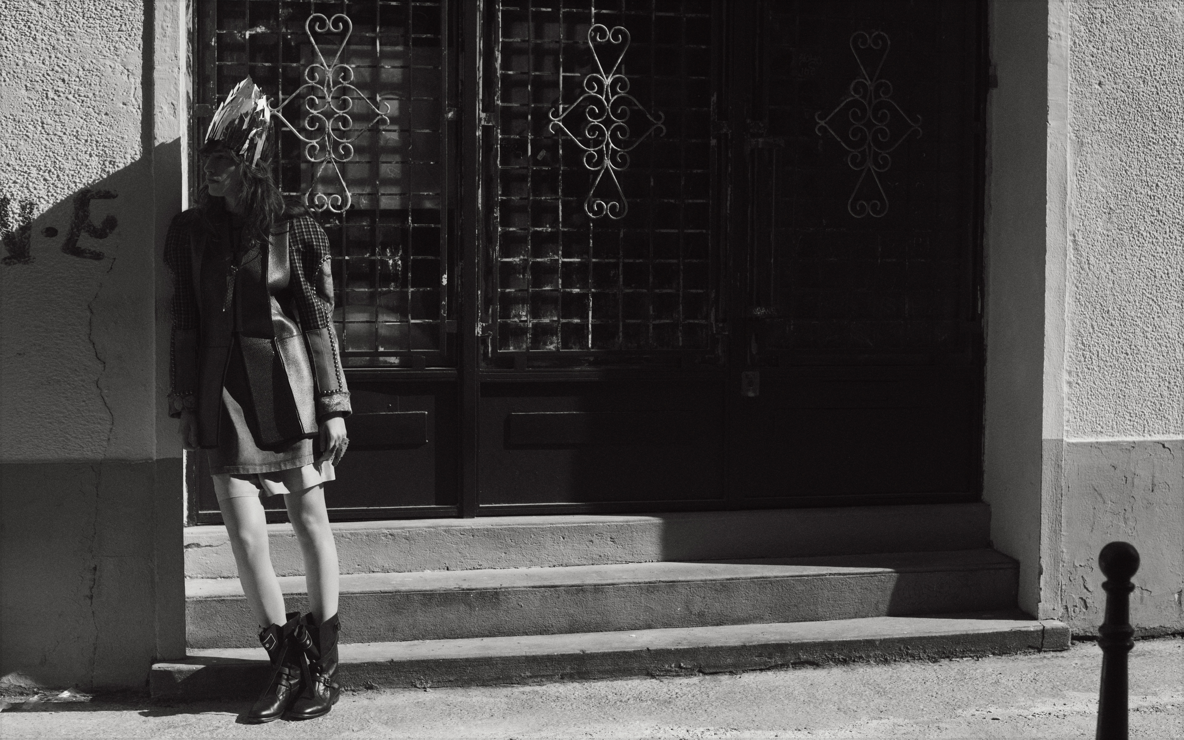 Monochrome fashion portrait of a model wearing an ornate crown and dark boots leaning against an entryway by Eminente Creative Production