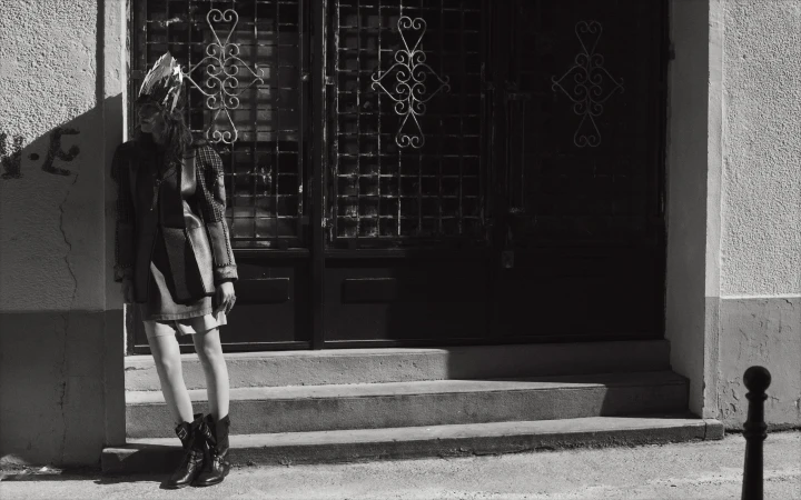 Monochrome fashion portrait of a model wearing an ornate crown and dark boots leaning against an entryway by Eminente Creative Production